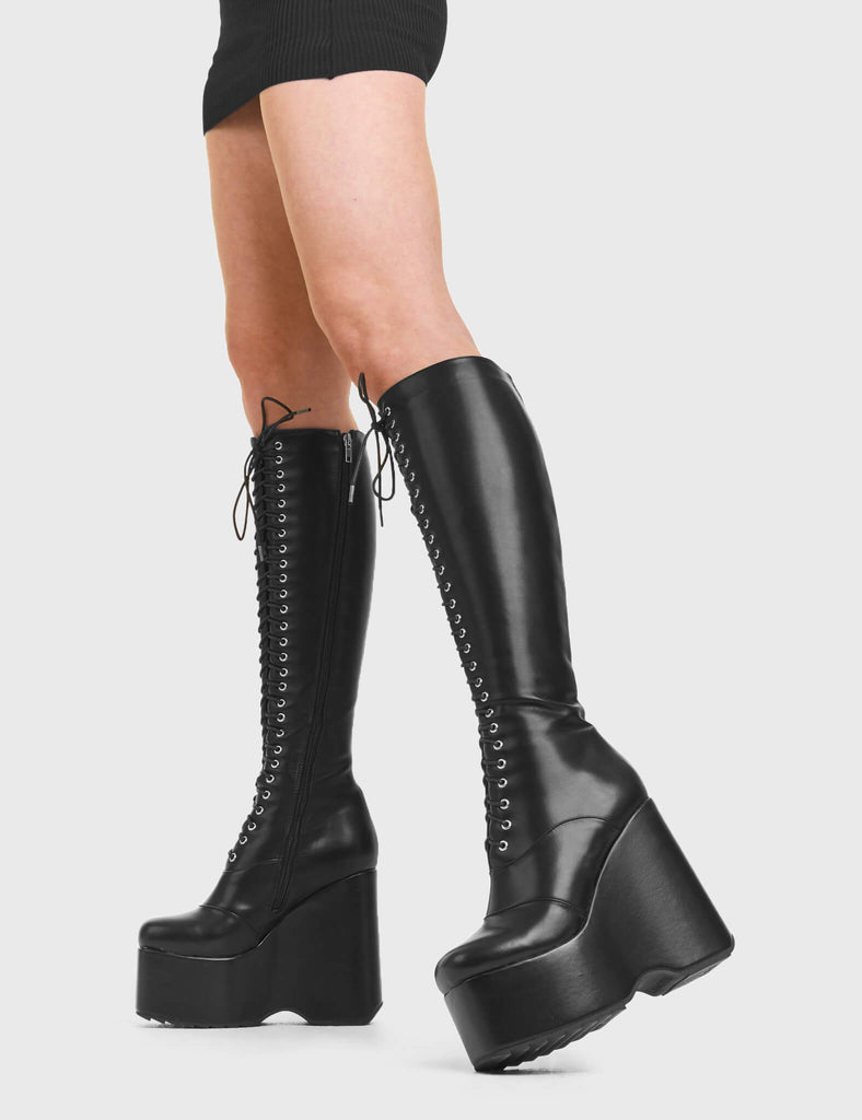 ICONIC Kiss CIty Chunky Platform Knee High Boots in Black faux leather. These platform boots feature a black lace up design with a platformed wedge. Made with eco-friendly materials and 100% cruelty-free, these platform boots are as ethical as they are chic. - Platform Height - Knee high length - Black lace up - Rounded toe - High Heel - 100% vegan SKU: LMF 3545 - BlackPU