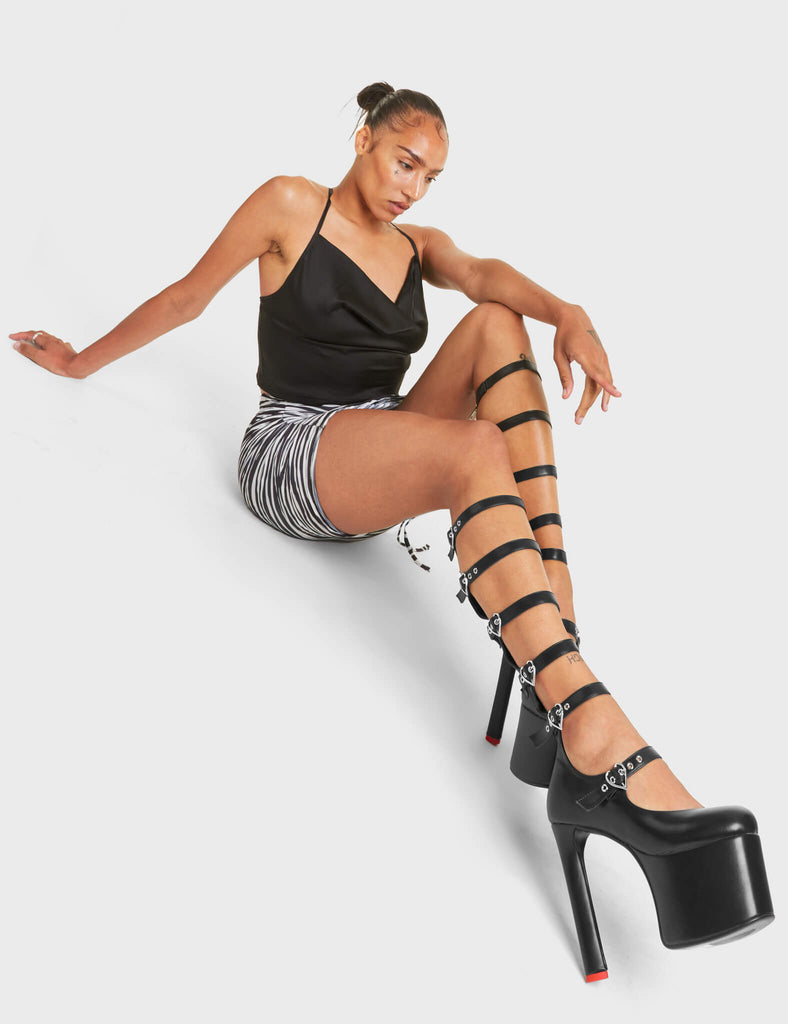 ROYAL TEA
 
 Still Reigning Platform Knee High Boots in Black faux leather. These vegan Boots feature siz adjustable white straps with silver heart shaped buckles and silver eyelets with high heel that features a red heart at the bottom. Walk like royalty.
 
 - Platform Height: 6 CM
 - Heel Height: 14 CM
 - Six Adjustable Straps
 - Cut-out Design
 - Knee High Length
 - Silver Heart Buckles
 - Silver Eyelets
 - Platform Sole
 - Round Toe
 - 100% Vegan
 
 SKU: LMF 4645 - BlackPU